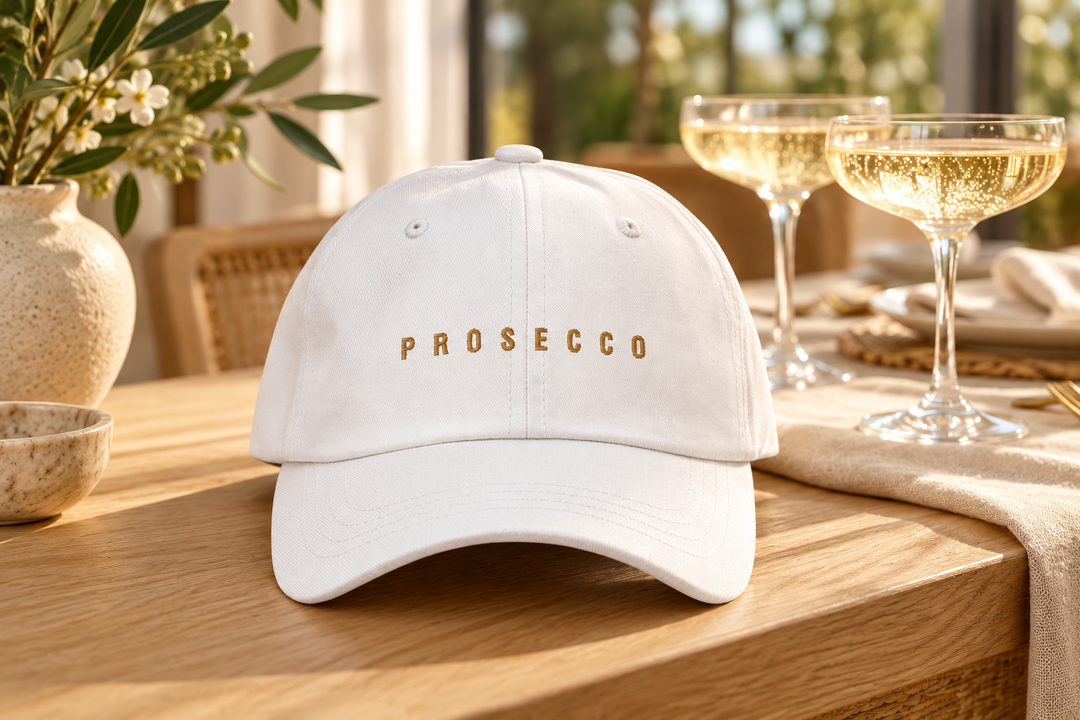 White Prosecco cap with gold embroidery beside sparkling wine glasses